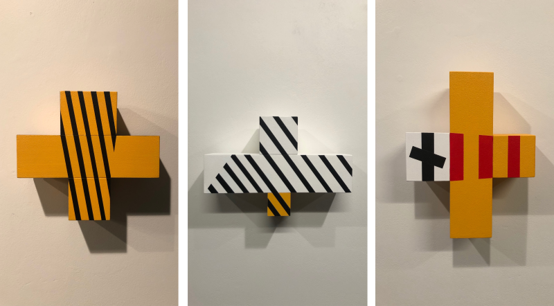 3 wooden sculptures of crosses with varying colours geometric designs